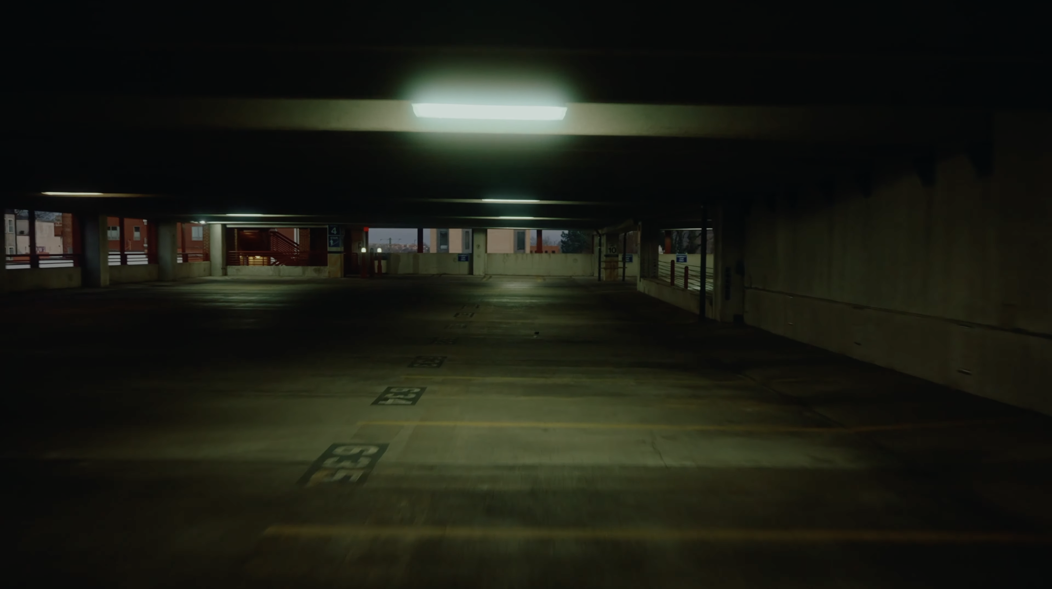 An empty concrete parking garage recedes into darkness beneath fluorescent lights.